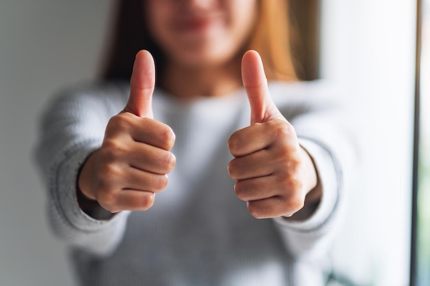 Photo closeup image of a young woman making and showing thumbs up hand sign