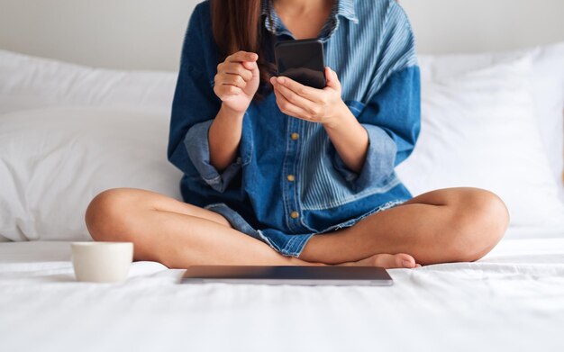 白いベッドに座って携帯電話を使用して見ている若い女性のクローズアップ画像