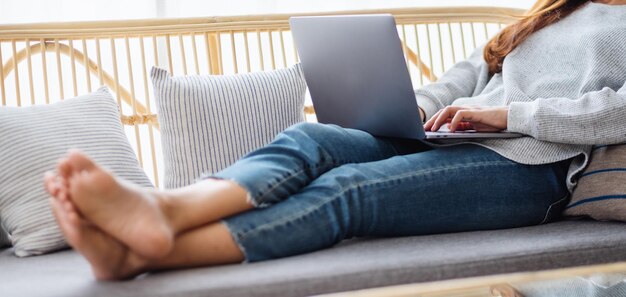 Closeup image of a young woman using and working on laptop computer while lying on a sofa at home