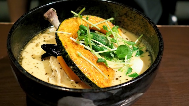 Крупным планом изображения супа карри желтого цвета с курицей, свининой и овощами в миске, которые известны