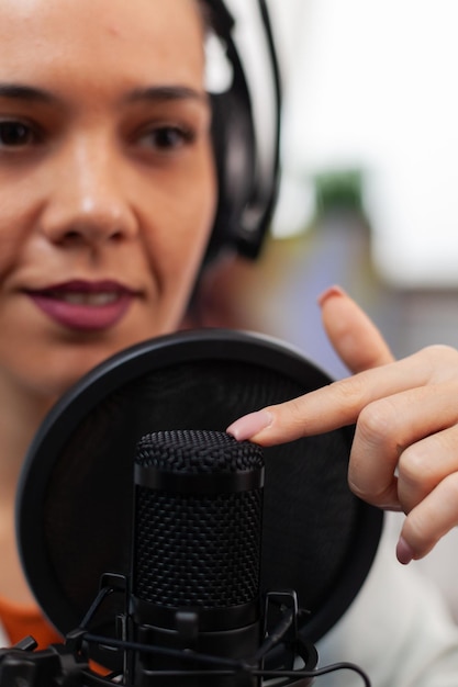 Closeup of influencer with headphones testing microphone sound.\
woman content creator touching audio equipment with index finger.\
sound check for online podcast streaming on social media.