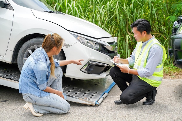 クローズ アップ保険会社の役員は、被害者の女性が彼女の車の背景に損傷を指摘するに従って、作業リストのクリップボードに修理のリストを投稿します。