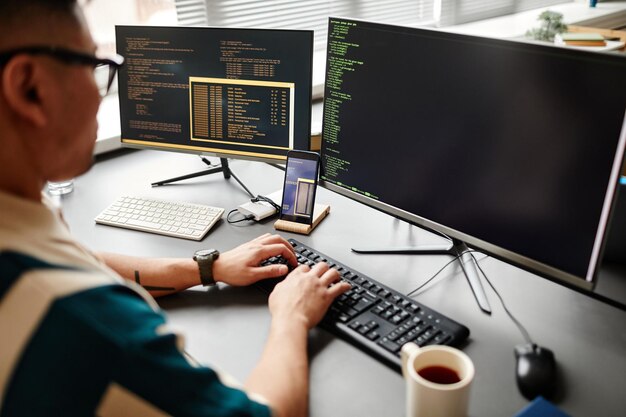 closeup of it developer typing on keyboard with programming code on computer screen while working in