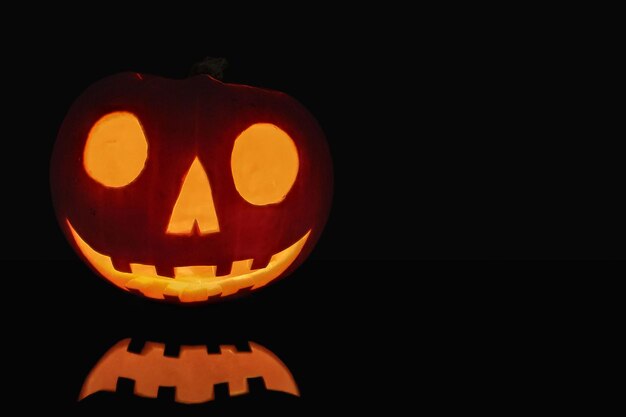 Closeup on a Jack O' Lantern lit in the dark and reflecting on a black surface in front of it