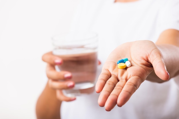 Closeup jonge Aziatische vrouw houdt pillen in de hand, klaar om medicijnen te nemen met een glas water