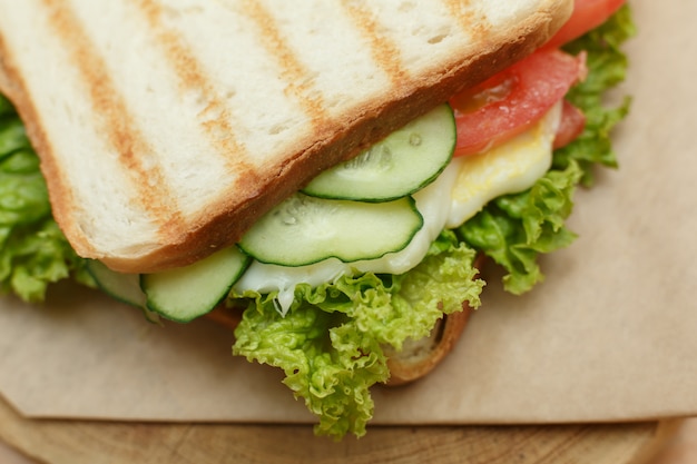 Closeup juicy sandwich with bacon, fresh vegetables, green salad and dark lines after grill