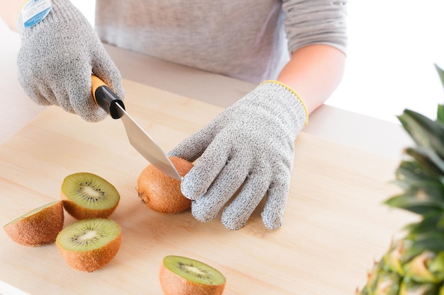 Primo piano di un bambino che taglia i kiwi con i guanti su una tavola di legno