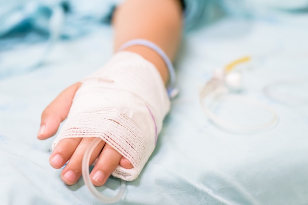 Closeup kid hand sleeps on a bed in hospital with saline intravenous.