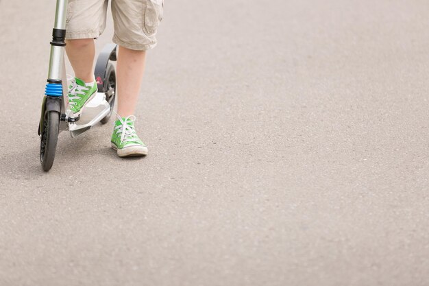 晴れた夏の日のライフスタイルの概念で公園でスクーターに乗る少年のスクーターの子供の足のクローズアップ