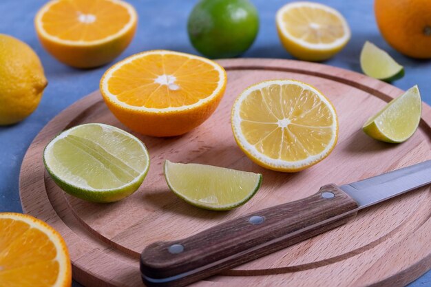 Foto primo piano di un coltello da cucina e di agrumi maturi interi e tagliati su un tagliere di legno rotondo n