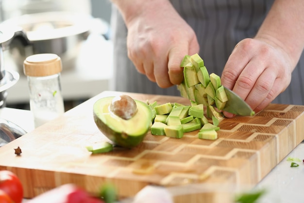 Closeup of knife with avocado slices on cutting board at home