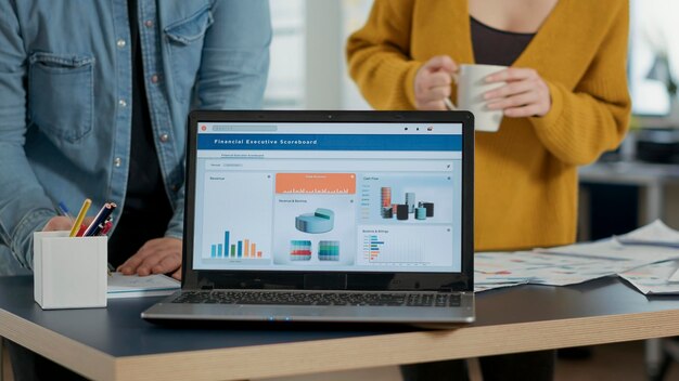 Photo closeup of laptop screen with business mangement software showing moving charts and statistics on desk in busy startup office. selective focus on portable computer with enterprise resource planning.