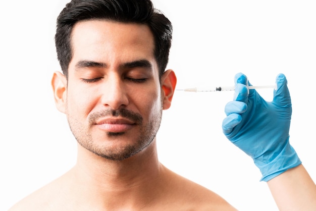 Closeup of latin male model getting an injection on his face by a doctor on white background