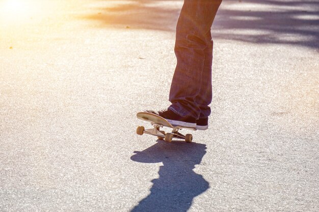 Gambe del primo piano dell'adolescente che gioca uno skateboard sulla strada del parco pubblico.