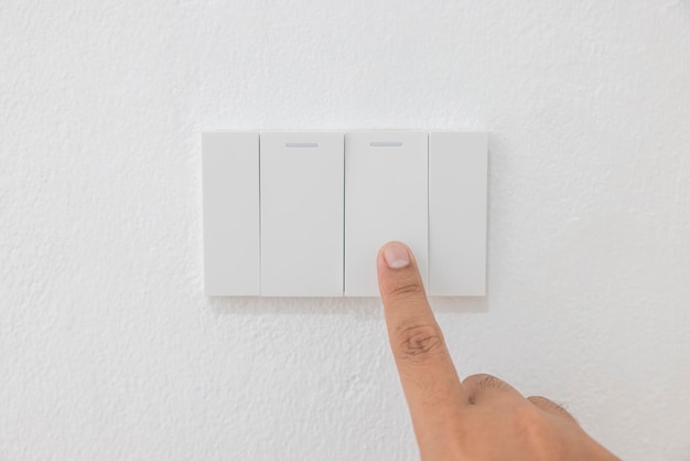 Closeup light switch of a male finger will turn on or off a light switch with white wall at home white plastic mechanical switch mounted Energy energy save electricity copy space