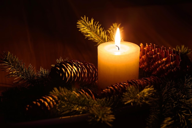 Closeup of a lit candle surrounded by pine cones in a dark Christmas setting