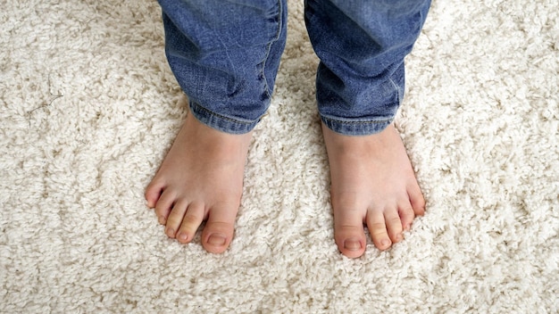 Closeup of little barefoot boy standing on soft white carpet and moving toes