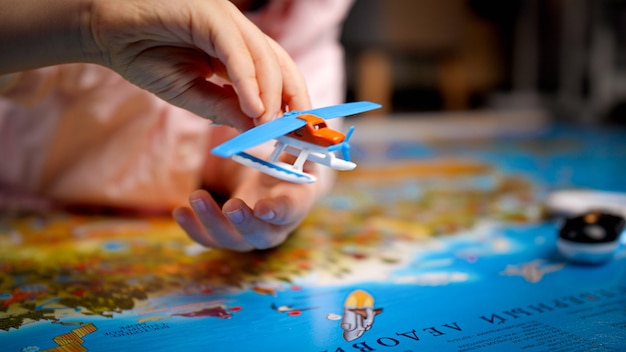 Closeup of little boy playing with small toy airplane on big world map. Concept of travel, tourism and child education. Kids exploration and discovery.