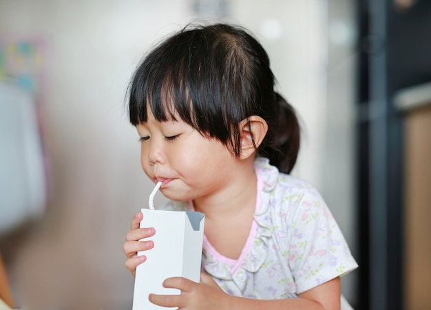 藁を持つ牛乳を飲む小さな女の子の拡大写真。