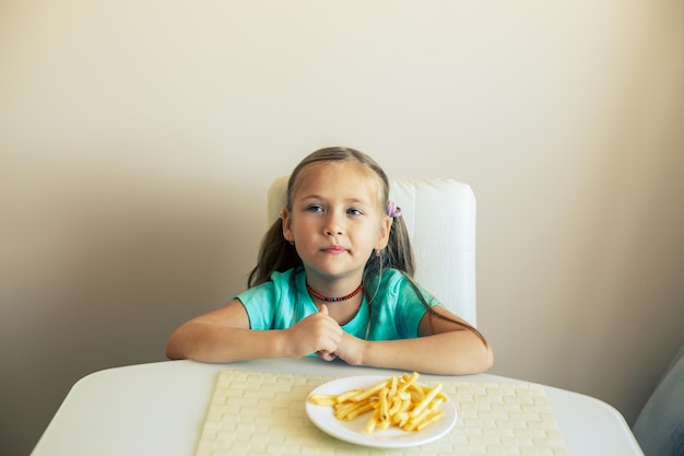 Closeup of a little girl eating french fries at the kitchen