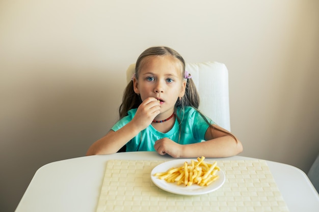 Photo closeup of a little girl eating french fries at the kitchen