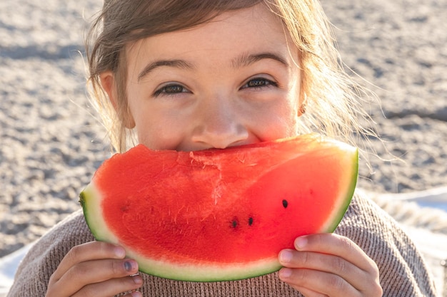 Closeup little girl eats watermelon on the beach