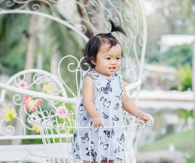 Closeup little girl stand on steel bicycle basket for decorate in the garden background with smile face