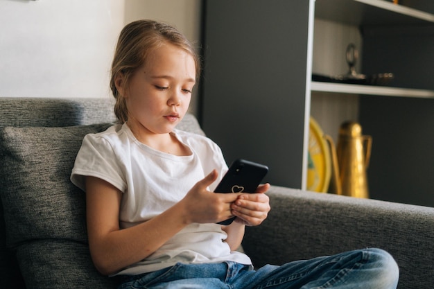 Closeup of little girl talking on video call by mobile phone in living room sitting on cozy sofa