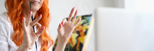 Closeup of lovely female artist showing ok sign with fingers looking on laptop cheerful painter