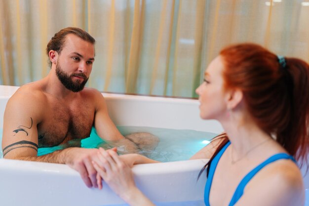 Closeup of loving young couple talking and having fun sitting in double hot bathtub with hydromassage at luxury spa salon