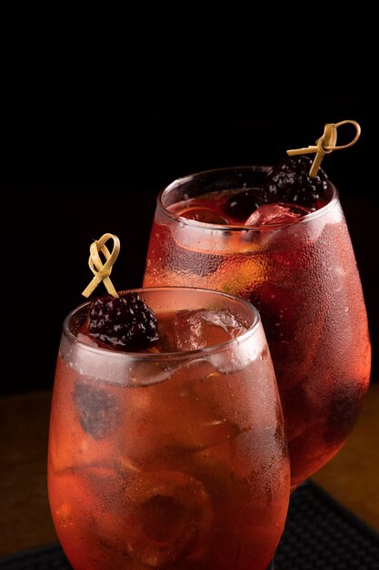 Closeup macro on two cocktail glasses with rosato rose wine and berries as garnish and ice isolated on wooden table and black background in focus