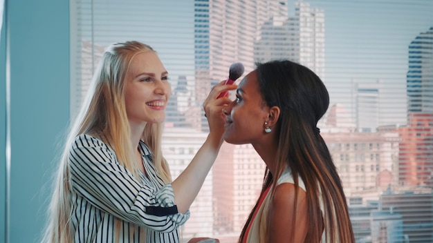 Photo closeup of makeup artist applying makeup on black model with skyscrapers in the background they prep...