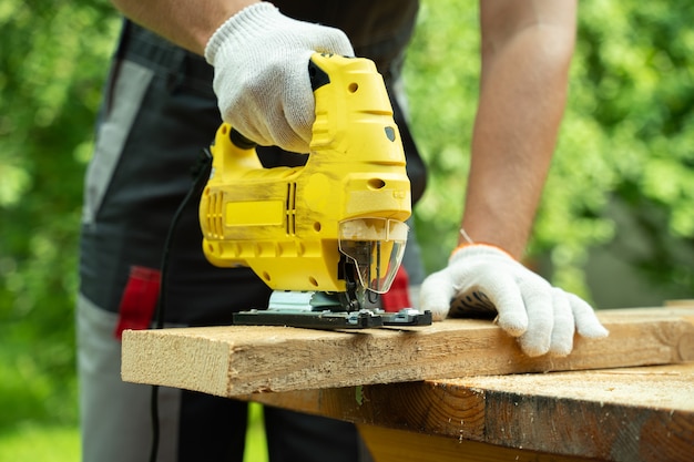 Closeup male carpenter cuts a wooden board using an electric jigsaw