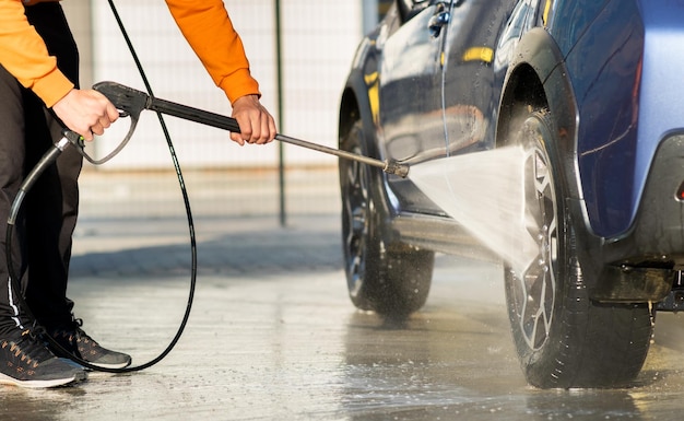 Primo piano del conducente maschio che lava la sua auto con getto d'acqua ad alta pressione senza contatto nell'autolavaggio self-service.