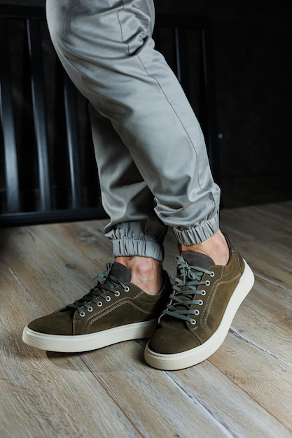 Closeup of male feet in green leather shoes A young man is standing in leather stylish green sneakers in gray jeans Summer men's shoes Casual street style