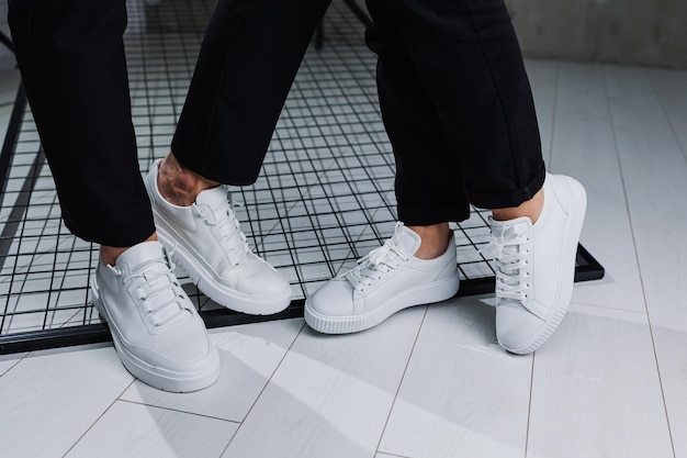 Closeup of male and female legs in black pants and white casual sneakers Summer men's and women's leather shoes