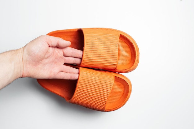 Closeup of male hand holding pair of orange slippers on white background