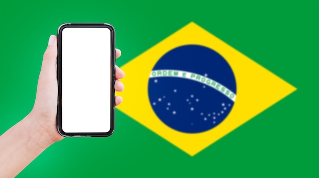 Closeup of male hand holding smartphone with blank on screen on background of blurred flag of Brazil