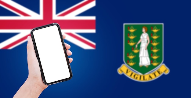 Closeup of male hand holding smartphone with blank on screen on\
background of blurred flag of british virgin islands