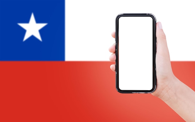 Closeup of male hand holding smartphone with blank on screen on background of blurred flag of Chile