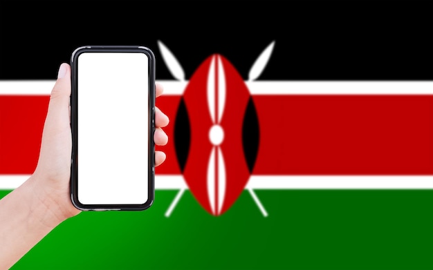 Primo piano della mano maschile che tiene smartphone con schermo vuoto sullo sfondo della bandiera sfocata del kenya