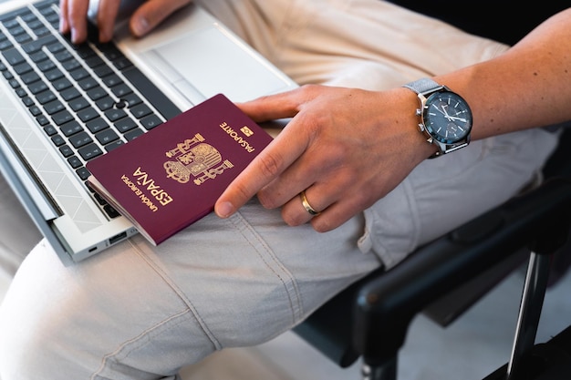 Closeup male hand holding spanish european passport while using\
computer laptop travel concept