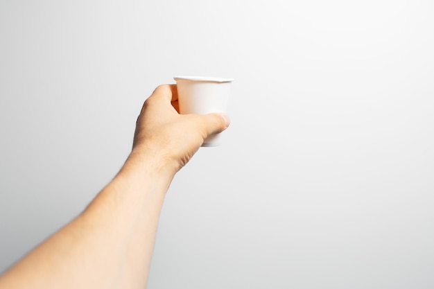 Photo closeup of male hand holding white paper cup of coffee takeaway on grey