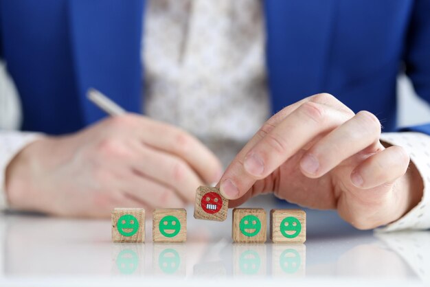 Closeup of male hand holding wooden cubes with angry emoji man giving negative feedback service