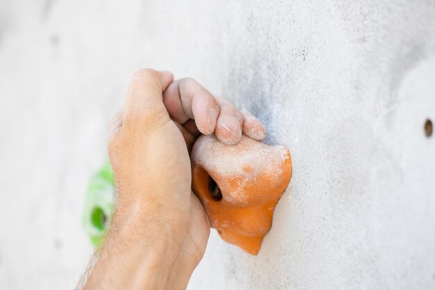 Closeup of a male hand smeared with magnesium powder grabbing a hold of a climbing wall