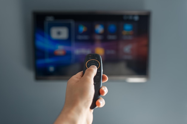 Photo closeup of male hand using remote of modern smart tv on background of television