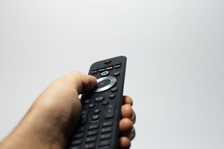 Closeup of male hand using tv remote control on grey background.