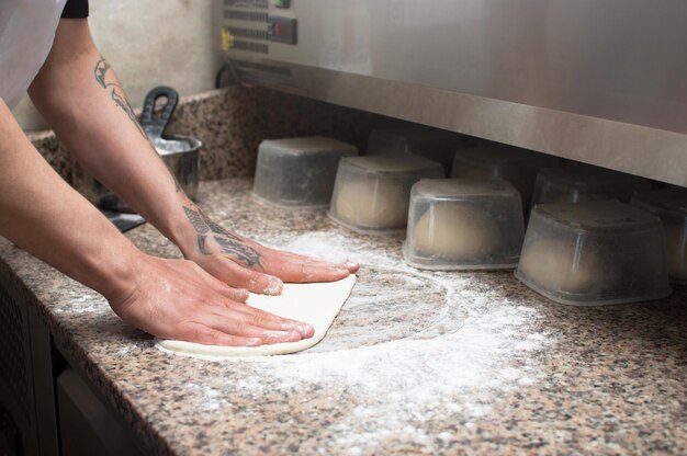 Foto primo piano delle mani maschili panettiere impasta pasta per pizza cruda fast food consegna della pizza