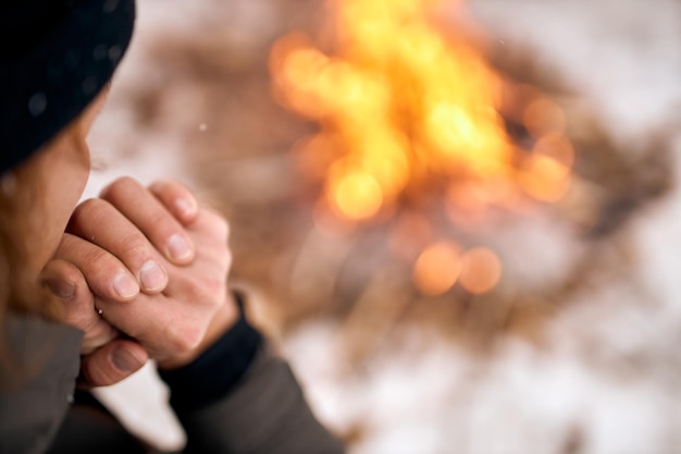 Primo piano mani maschili e faccia uomo seduto accanto al falò pensando sognando in contemplazione calma fuoco da solo sullo sfondo