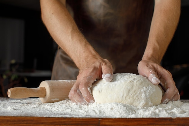 Foto primo piano mani maschili impastare la pasta su uno sfondo scuro panetteria pubblicità foto concetto processo i